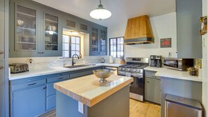 Une cuisine moderne avec des meubles gris, un îlot central en bois, une cuisinière, un four à micro-ondes et un évier.