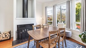 A dining area with a fireplace, wooden table, chairs, and large windows with curtains. - Quiet Capitol Hill Bungalow w/ Wi-Fi & Laundry (Seattle)