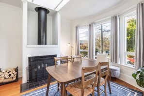 A dining area with a fireplace, wooden table, chairs, and large windows with curtains.