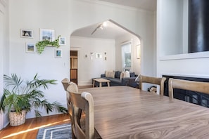 Een eethoek met een houten tafel en stoelen, een potplant en ingelijste foto’s aan de muur.
