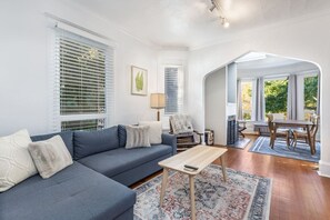 A living room with a sofa, a coffee table, a dining table with chairs, and a fireplace.