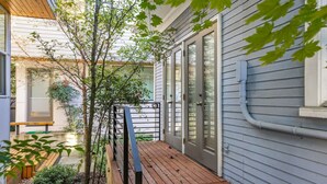 A wooden deck with a metal railing, a sliding glass door, and a small garden area with trees and shrubs. - Quiet Capitol Hill Bungalow w/ Wi-Fi & Laundry (Seattle)