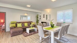 A modern living room with a brown sofa, white coffee table, and a dining area with a white table and grey chairs.