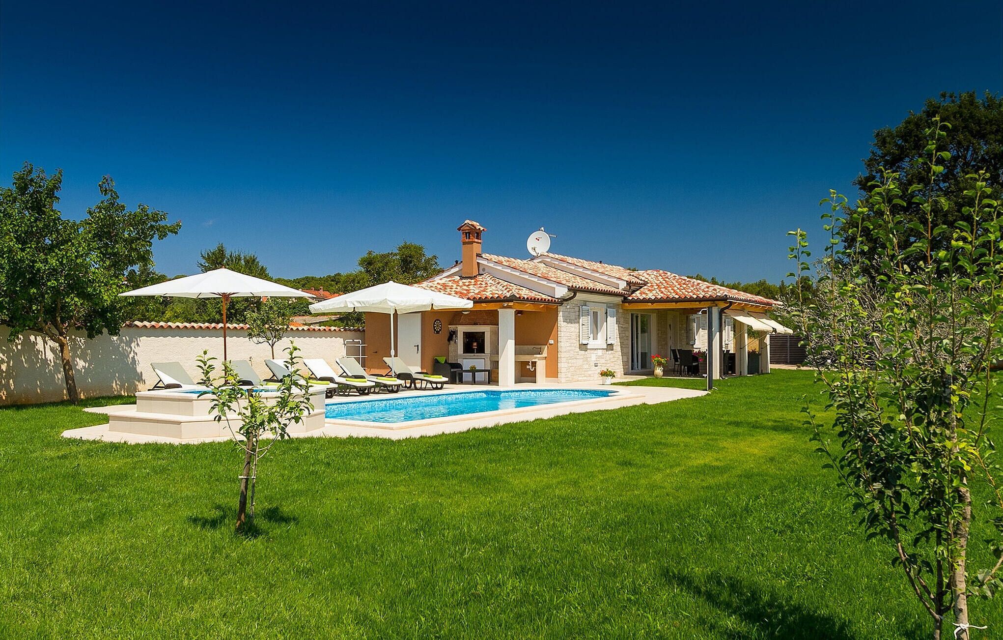 A house with a swimming pool, outdoor seating, and a well-maintained lawn.