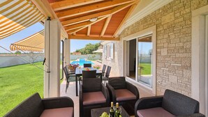 An outdoor patio with wicker furniture, a table with drinks, and a view of a swimming pool and garden.