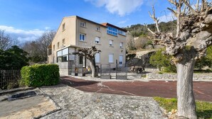 Edifici de dues plantes amb façana de pedra, entrada tancada per reixes i un carrer pavimentat que condueix a un cotxe vermell a l'exterior.