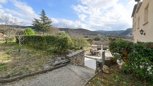 Un pati amb mur de pedra, una cadira de fusta i vistes als turons de l'entorn.