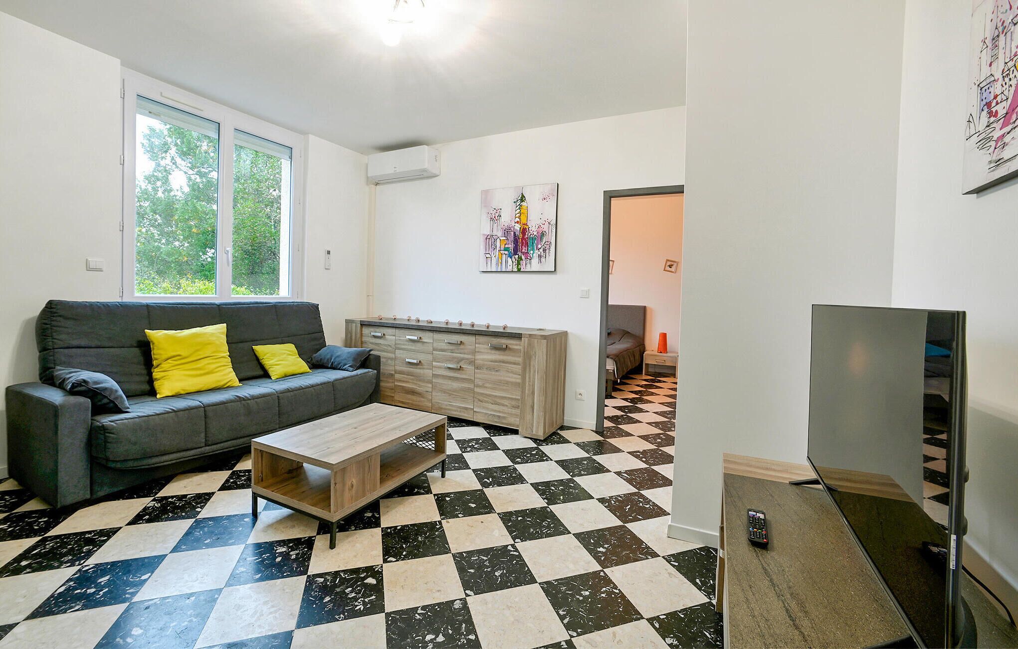 Een woonkamer met een grijze bank, een houten salontafel, een televisie en een geruit vloerkleed.