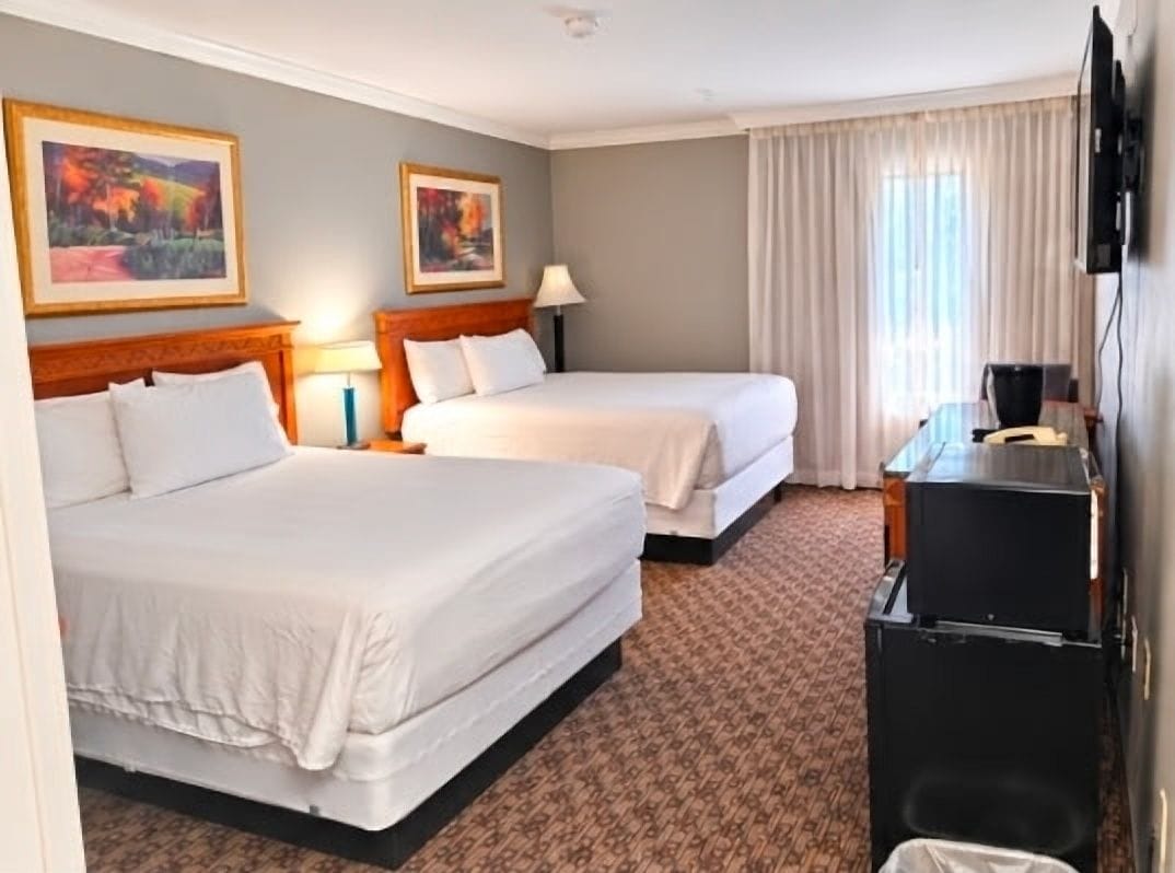 A hotel room with two beds, a television, a desk, and a window with curtains.
