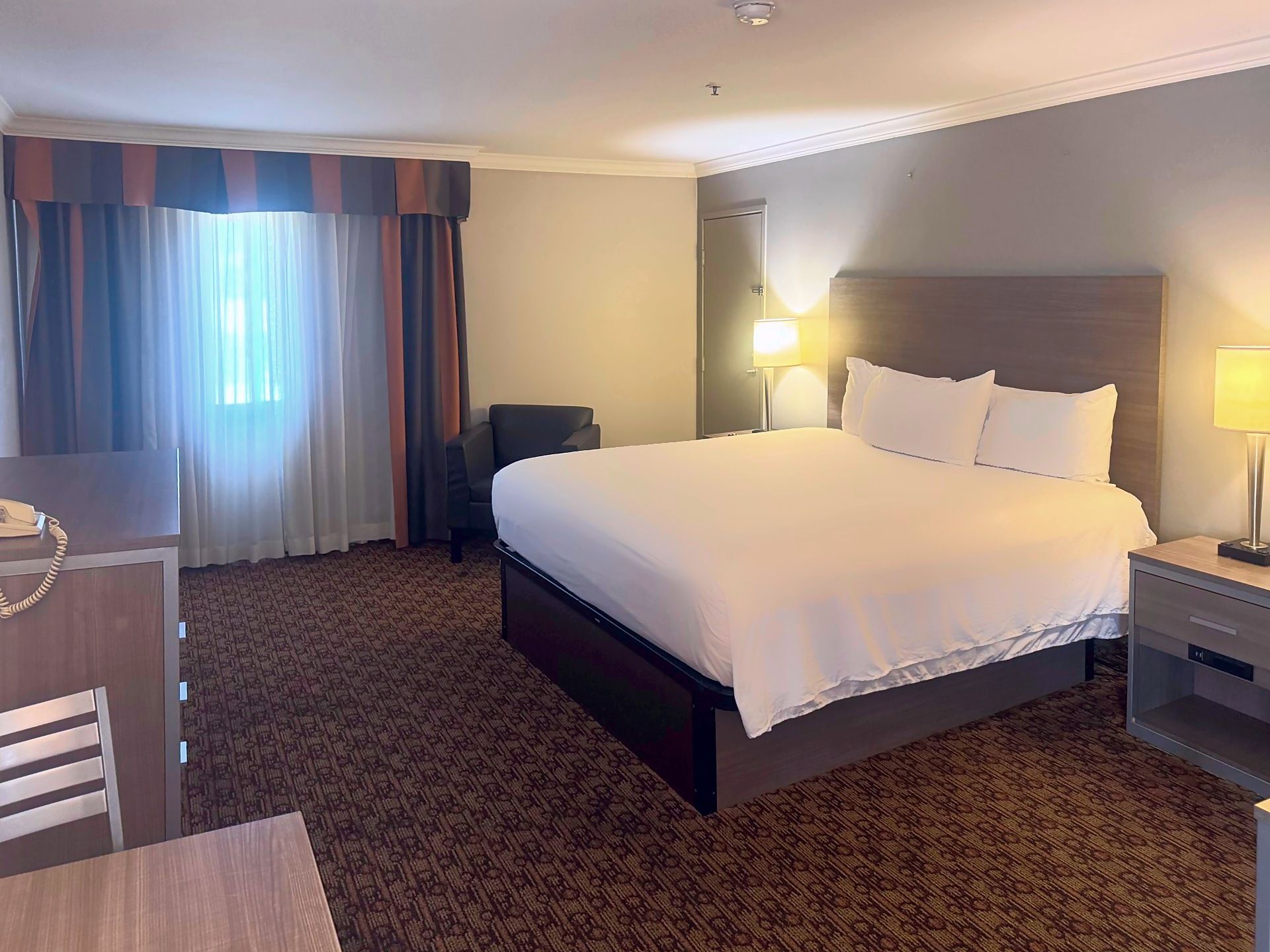 Habitación de hotel con una cama grande, un escritorio, una silla y una mesita de noche con lámpara.