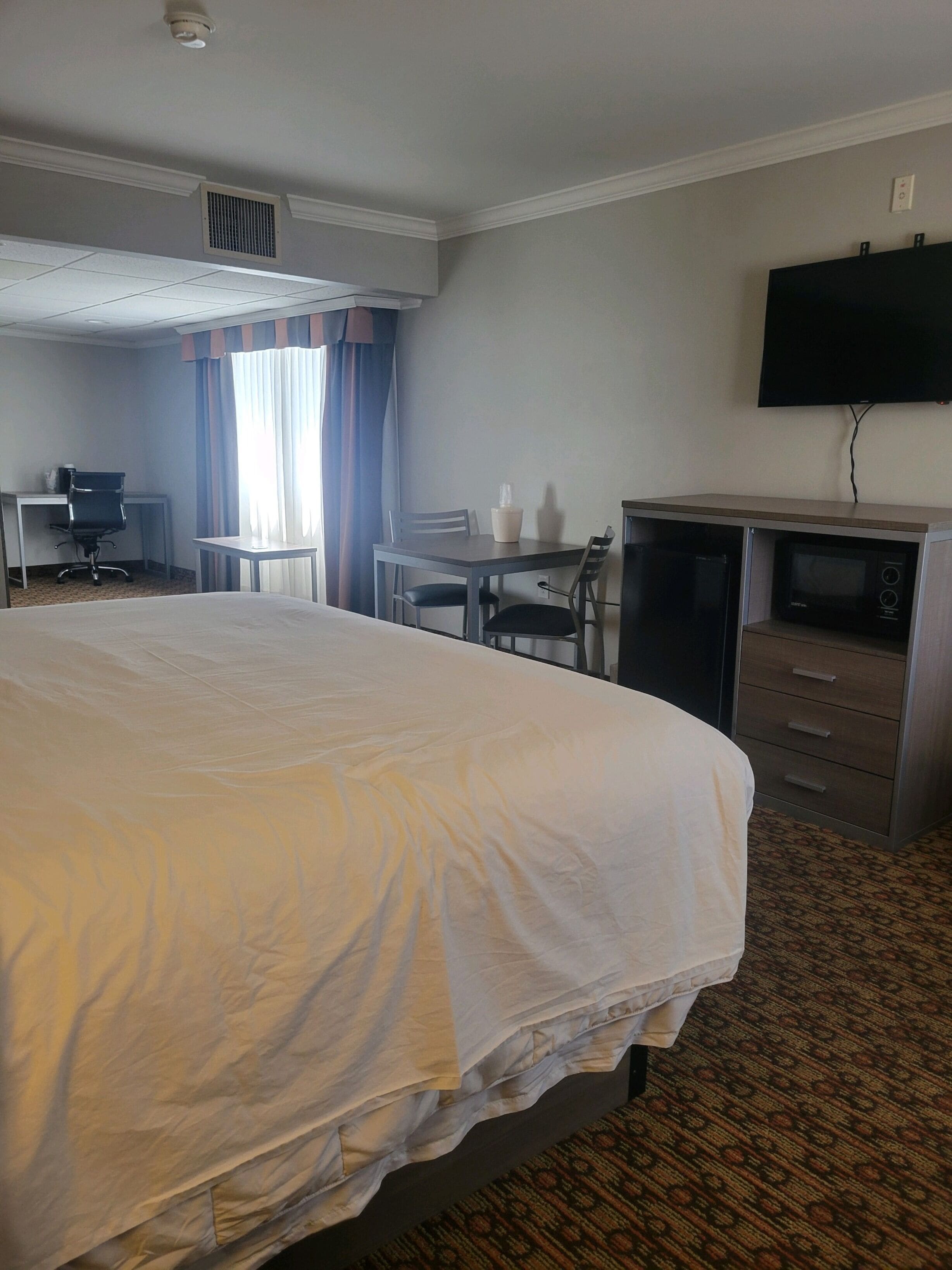 A hotel room with a large bed, a desk with a chair, a television, and a microwave.
