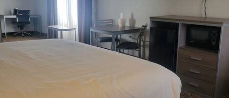 Quarto de hotel com uma cama grande, uma mesa com cadeira, televisão e micro-ondas.