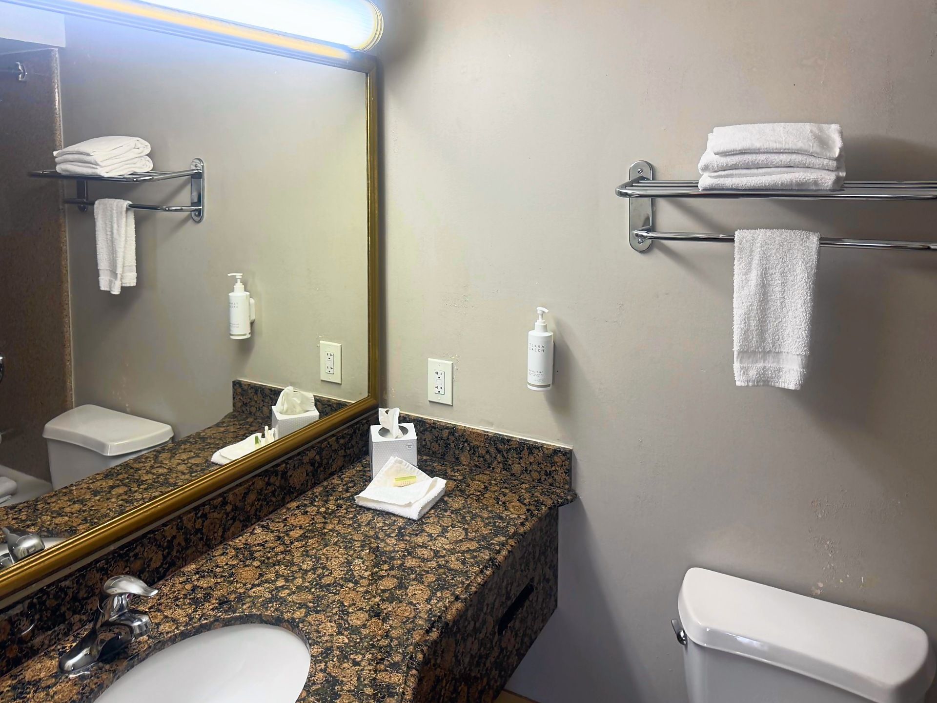 A bathroom with a granite countertop, a sink, a toilet, a mirror, and towel racks.