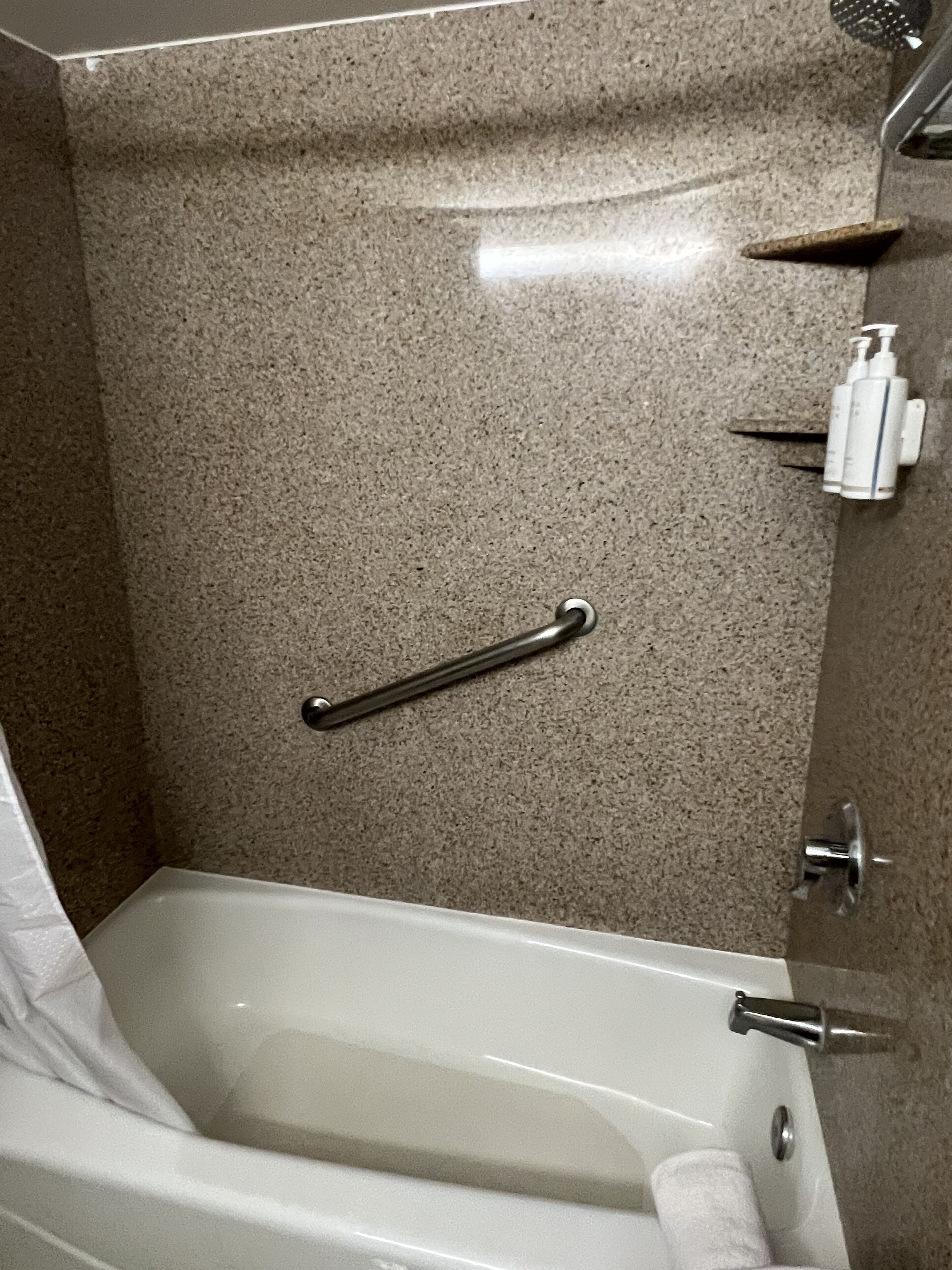 A bathroom with a bathtub, a handrail, a towel rack, and a showerhead.