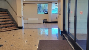 A hotel lobby with a tiled floor, a staircase, a reception desk, and a large glass door. - Hotel Xola (Moreno Valley)