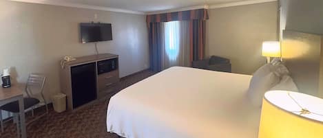 Une chambre d’hôtel équipée d’un lit, d’un bureau, d’une télévision, d’une chaise, d’une lampe et d’une fenêtre avec des rideaux.