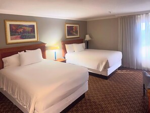 A hotel room with two beds, a nightstand with a lamp, and two framed paintings on the wall. - Hotel Xola (Moreno Valley)
