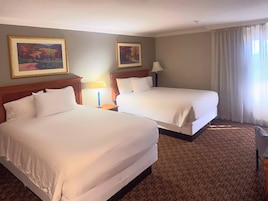 Habitación de hotel con dos camas, una mesita de noche con lámpara y dos cuadros en la pared.