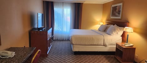 A hotel room with a bed, bedside lamps, a TV, a desk with a phone, and a window with curtains.
