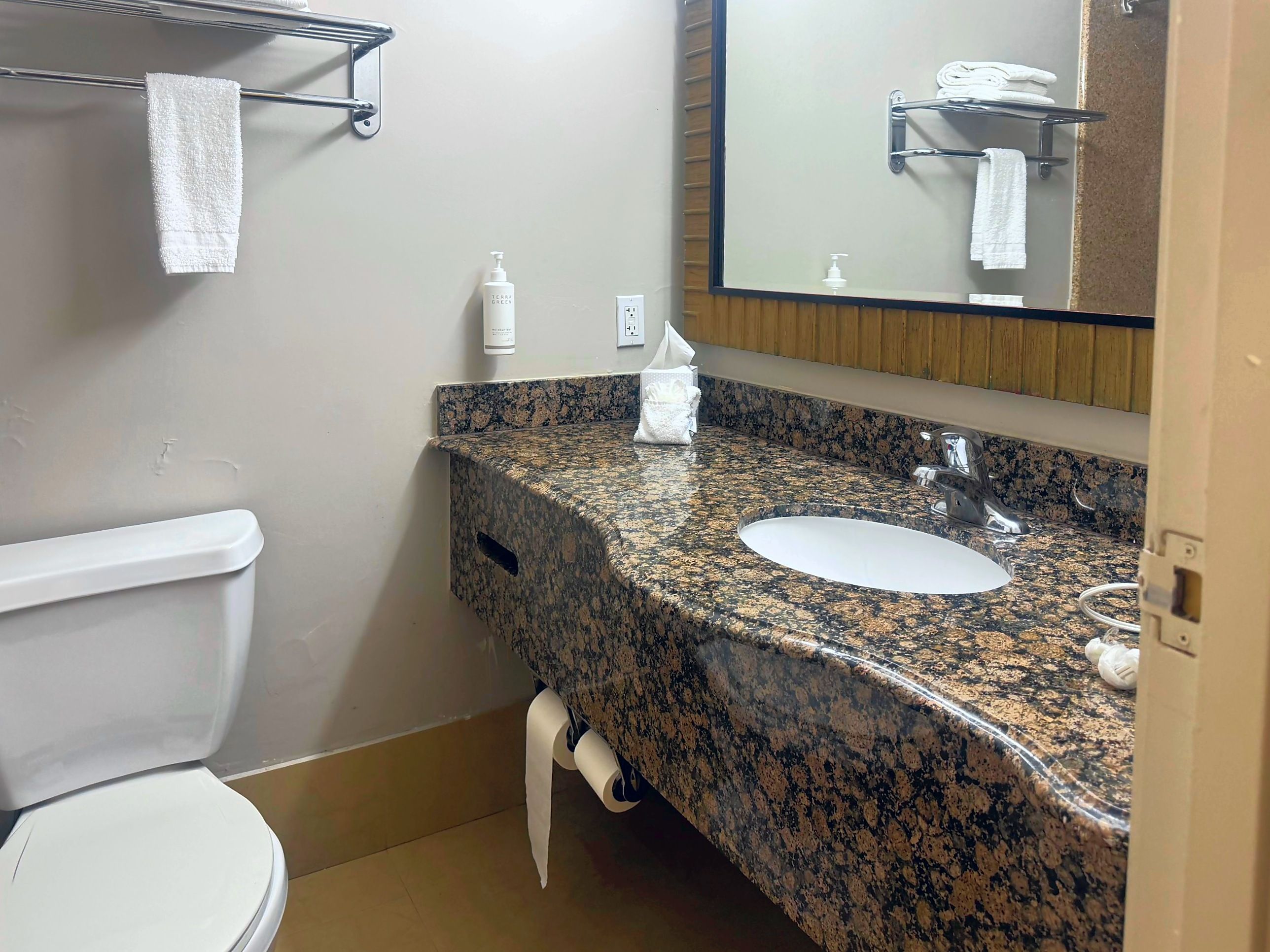 A bathroom with a toilet, sink, mirror, towel rack, and toiletries.