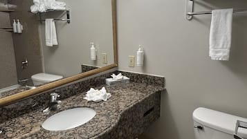 A bathroom with a granite countertop sink, a mirror, a toilet, and a towel rack.