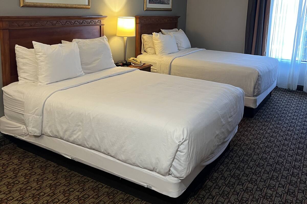 A hotel room with two beds, a nightstand with a lamp, and two framed pictures on the wall.