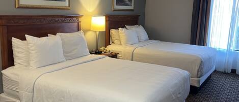 A hotel room with two beds, a nightstand with a lamp, and two framed pictures on the wall.