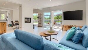 A modern living room with a blue sofa, a flat-screen TV, and a sliding glass door leading to an outdoor patio. - Nice home in Svetvincenat (Svetvincenat)