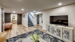 A spacious living area with a large TV, a staircase, and a dining area. - Quiet Comfort: 5 BR & 2.5 BA, 6 TVs, Pet Friendly (Radcliff)