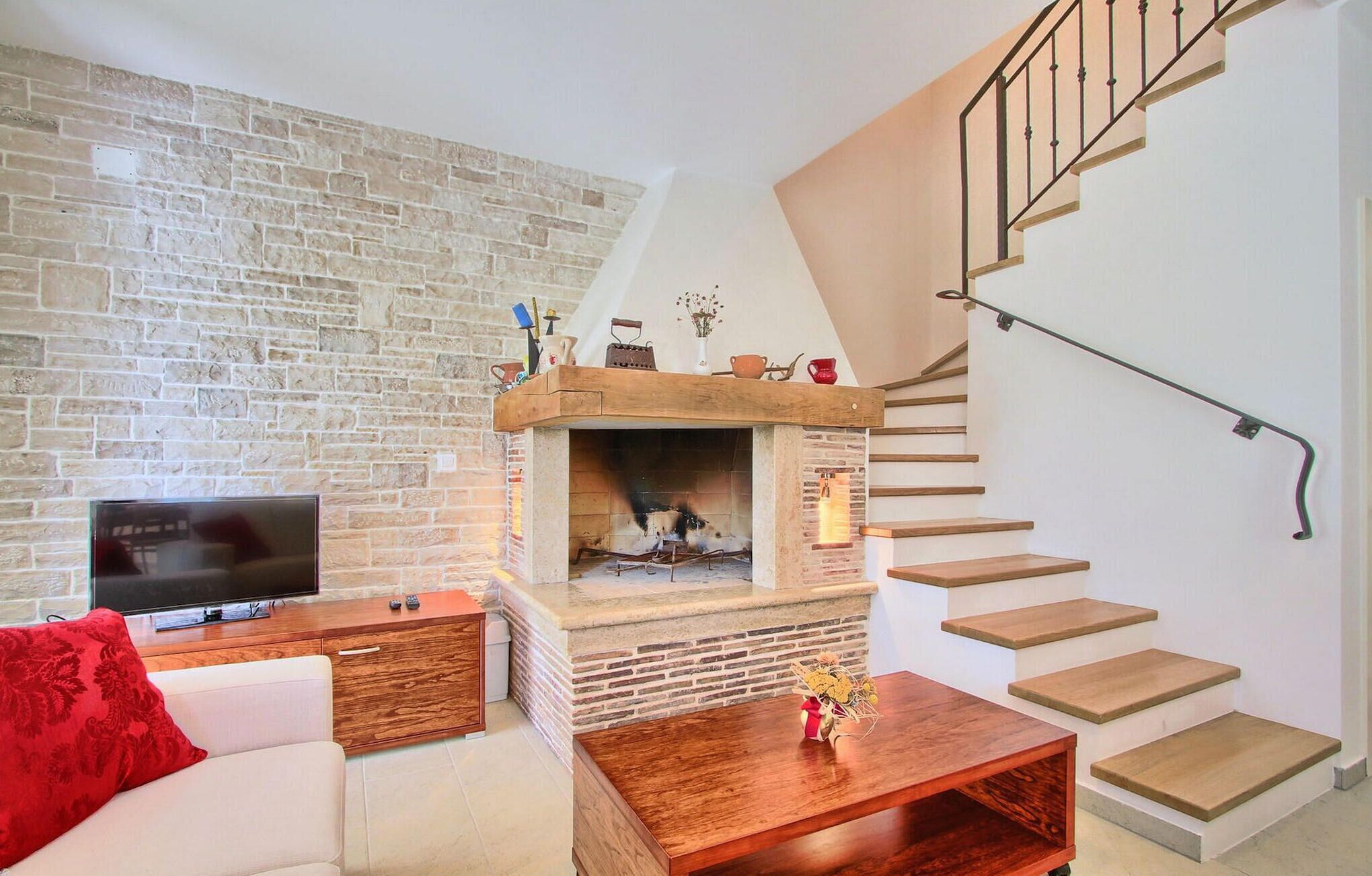 A living room with a stone wall, a fireplace, a wooden coffee table, a sofa, and a staircase.