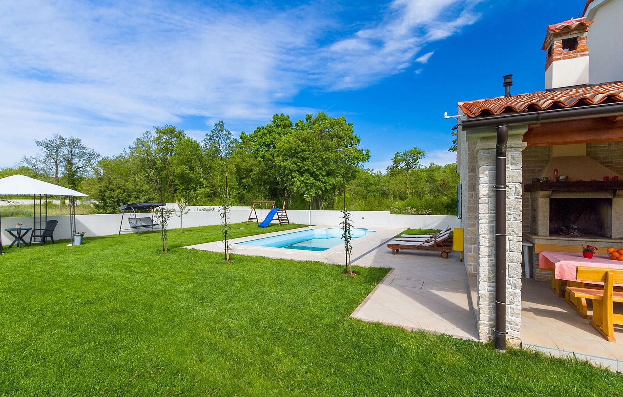 A backyard with a swimming pool, a covered patio area, and a stone fireplace.