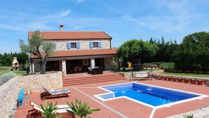 Une maison en pierre à deux étages, dotée d’une piscine, d’un espace salon extérieur et d’un mur en pierre.