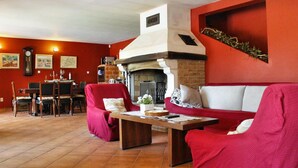 Un salon avec une cheminée, des murs rouges et un coin repas comprenant une table et des chaises.
