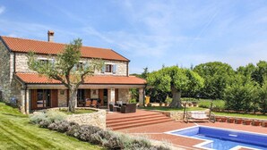 Une maison en pierre à deux étages, avec un toit en tuiles, une piscine et un patio aménagé avec du mobilier d’extérieur.