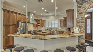 Una cocina con encimeras de granito, armarios de madera, un refrigerador de acero inoxidable y una pared decorativa de ladrillo.