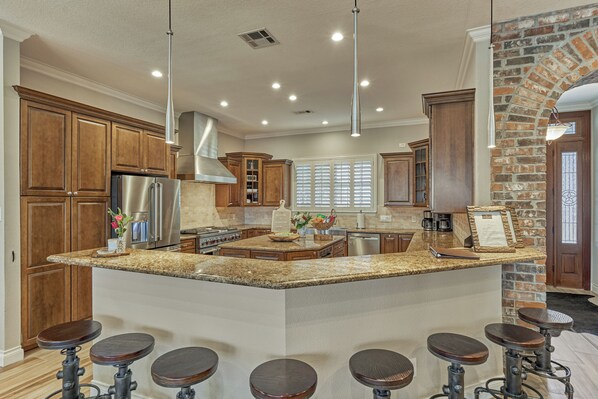 A kitchen with granite countertops, wooden cabinets, a stainless steel refrigerator, and a brick accent wall.