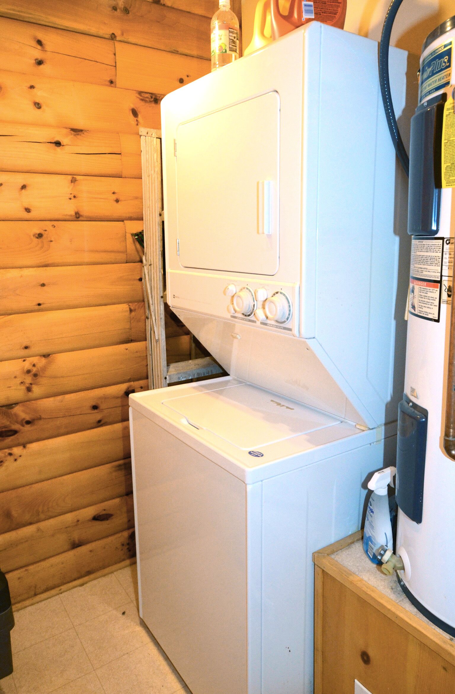 A compact laundry area with a washer and dryer, wooden walls, and a small cabinet with a water dispenser.