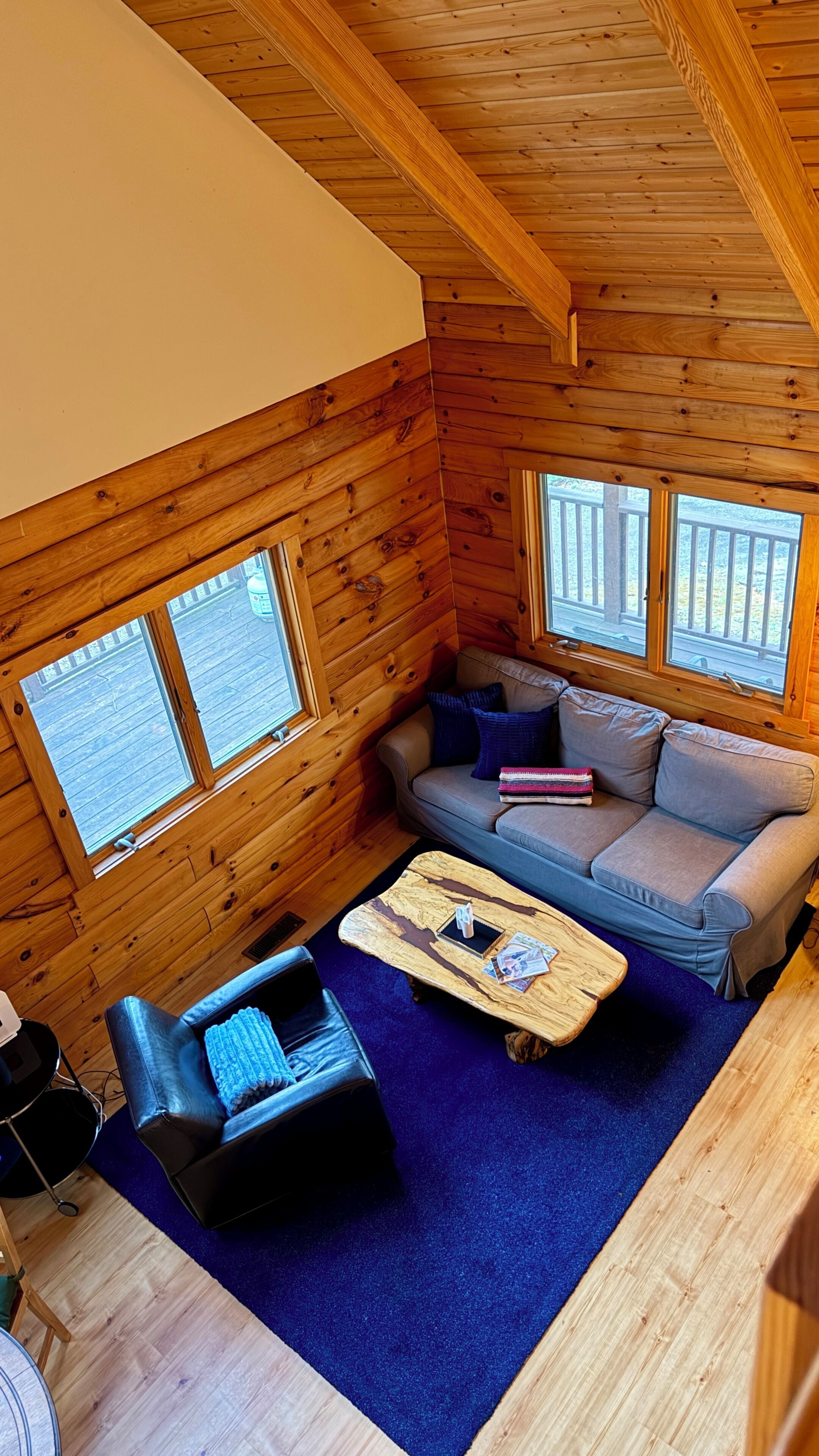 A cabin interior with a wooden ceiling, a sofa, a coffee table, and a chair.