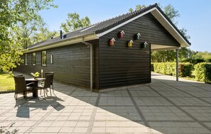 A wooden building with a covered patio area, a table with chairs, and a small garden.