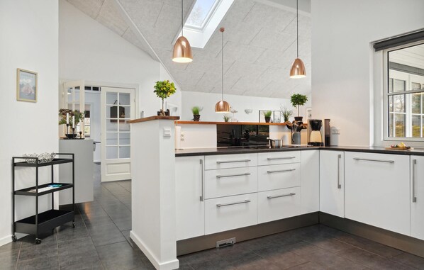 A modern kitchen with white cabinets, a black countertop, and two pendant lights. There are plants on the countertop and a small shelf above the sink. - Stunning home in Hadsund with sauna (Hadsund)