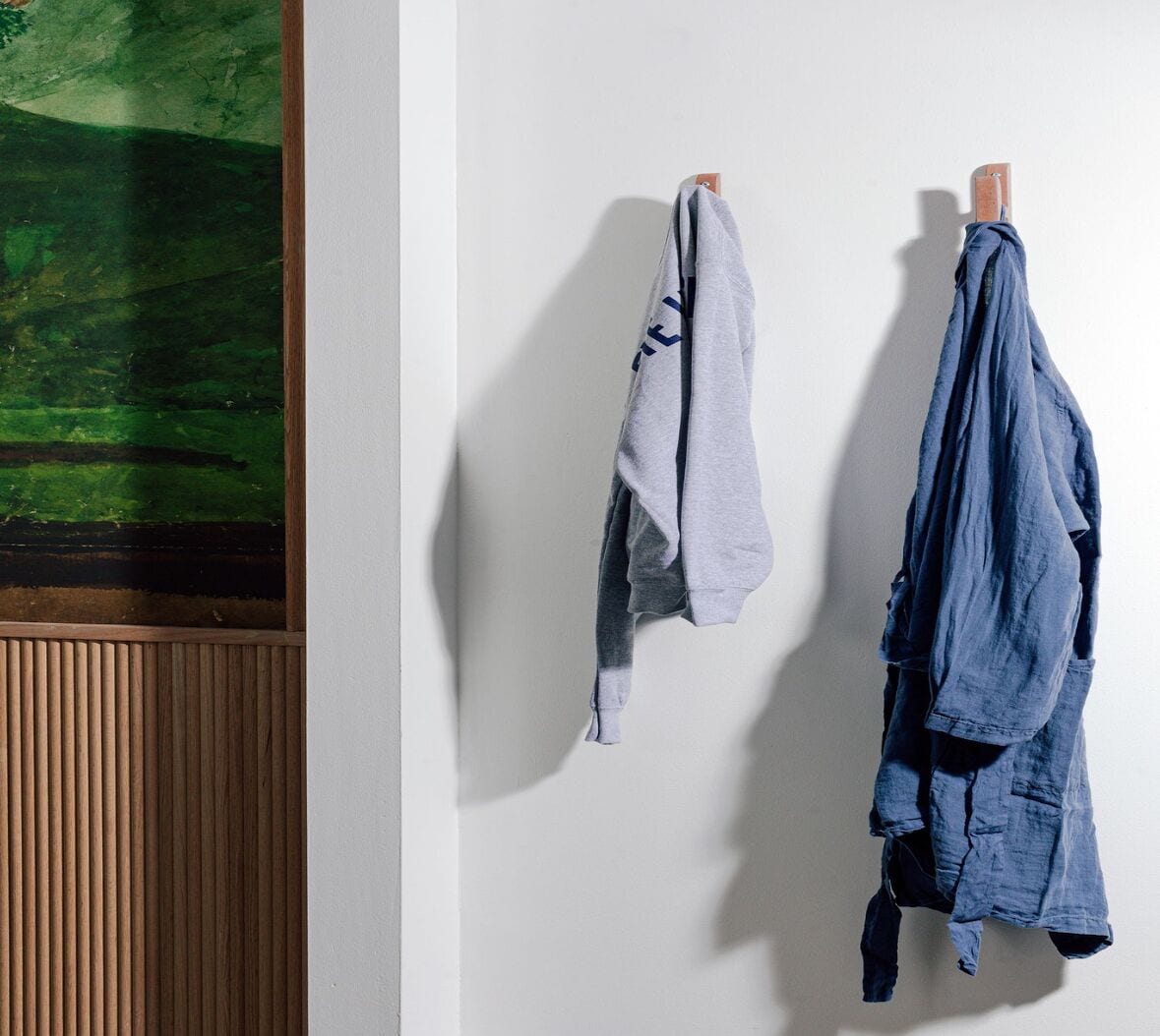 Une pièce avec un mur recouvert de lambris en bois, un tableau abstrait vert et deux vêtements suspendus à des cintres en bois.