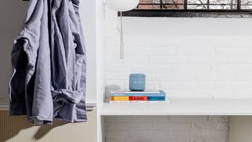 A room with a hanging plant, a stack of books, a blue container, and a black stool.