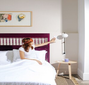 A bedroom with a bed, a bedside table with a lamp, and a framed picture on the wall. - Dye House (Providence)