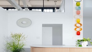 A reception desk with a wooden finish, a potted plant, and a wall-mounted circular light fixture. - Dye House (Providence)