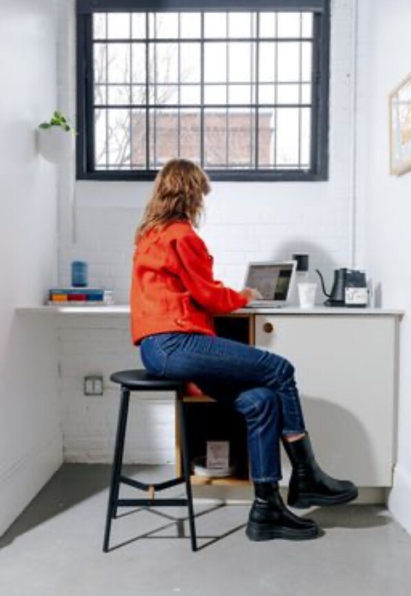 A person seated at a desk in a room with a window, a water dispenser, and a small plant. - Dye House (Providence)