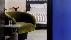 A room with a bed, a green armchair, a small round table with a glass, and a red lamp. - Dye House (Providence)