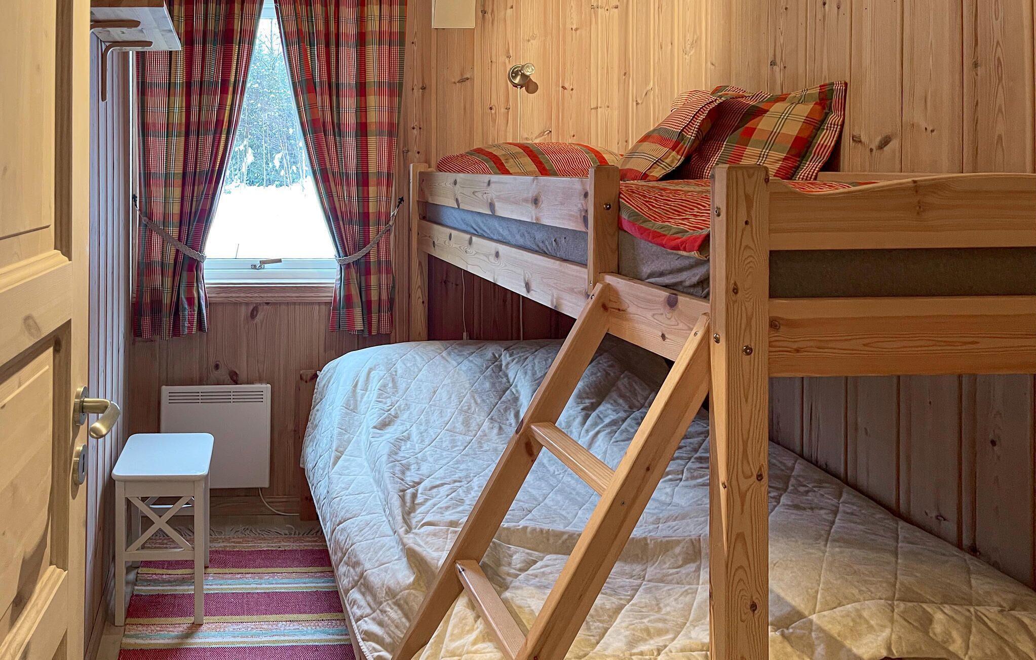 A wooden bunk bed room with a window, a small table, and plaid curtains.