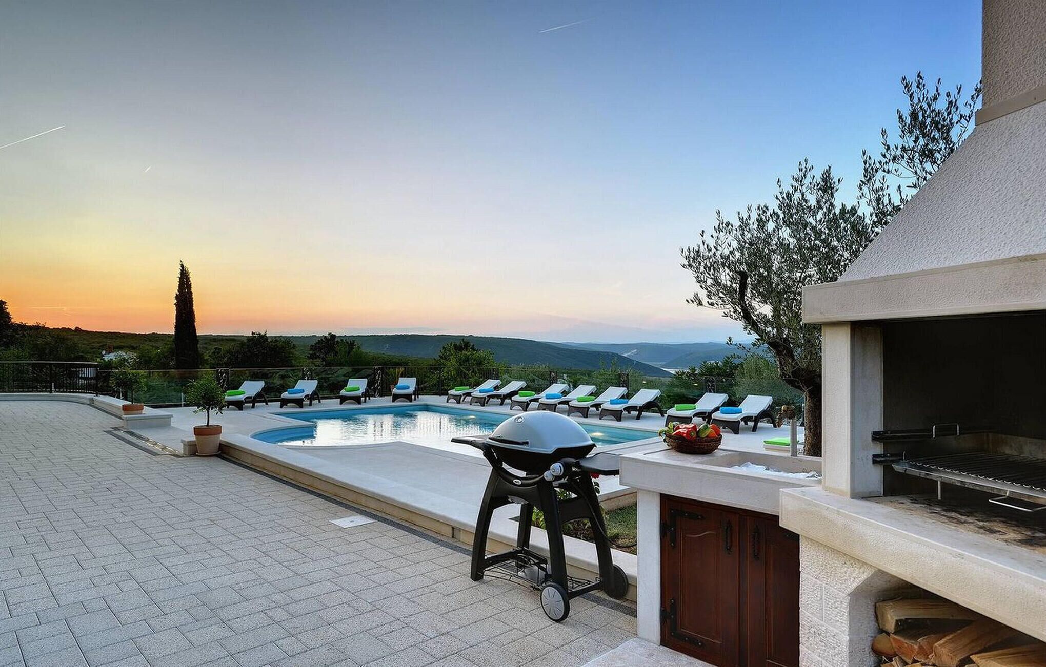 Un espace aménagé au bord de la piscine, avec des chaises longues, un barbecue et une vue sur le paysage.