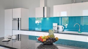 A modern kitchen with white cabinets, a blue backsplash, and a fruit bowl on the counter.