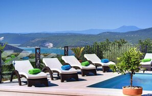 Un área junto a la piscina con sillones de descanso y vistas a un paisaje montañoso.